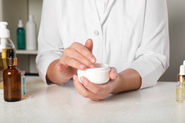 Dermatolog, kozmetik ürünlerini kapalı bir masada test ediyor.