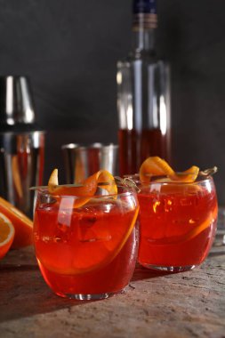 Aperol sprey kokteyli, buz küpleri ve gri desenli masada portakal dilimleri.