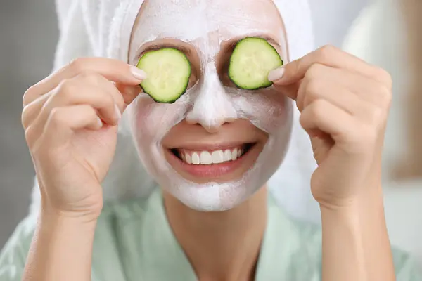Woman with face mask and cucumber slices on blurred background, closeup. Spa treatments