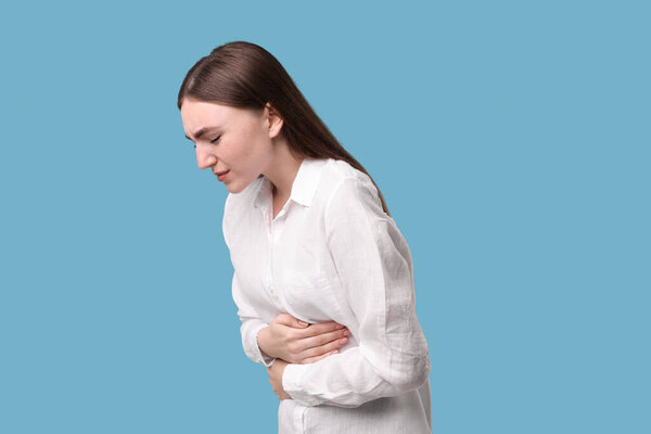 Young woman suffering from stomach pain on light blue background