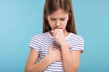 Açık mavi arka planda öksüren hasta kız.