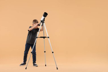 Küçük çocuk yıldızlara teleskopla bakıyor. Bej arka planda, mesaj için yer var.