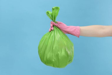 Açık mavi arka planda çöp dolu plastik poşet taşıyan kadın, yakın plan.