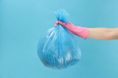 Açık mavi arka planda çöp dolu plastik poşet taşıyan kadın, yakın plan.