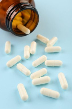 Açık mavi arka planda şişe ve vitamin kapsülleri, yakın plan