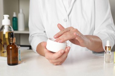 Dermatolog, kozmetik ürünlerini kapalı bir masada test ediyor.