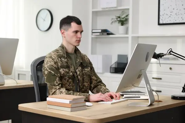Military education. Young student in soldier uniform learning at wooden table in room
