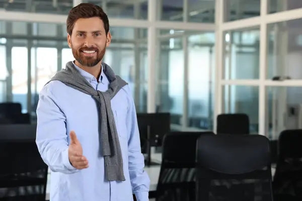 Happy man welcoming and offering handshake in office, space for text