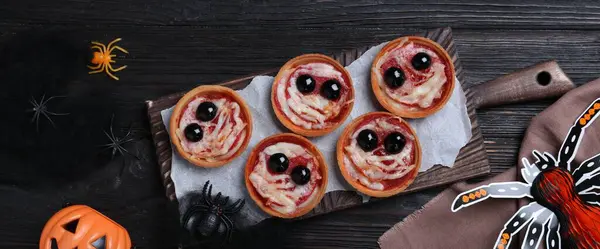 Cute monster tartlets served on black wooden table, flat lay with space for text. Halloween party food