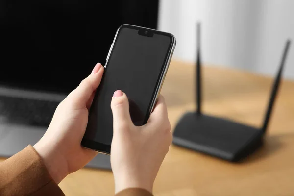 Woman with smartphone connecting to internet via Wi-Fi router at table indoors, closeup