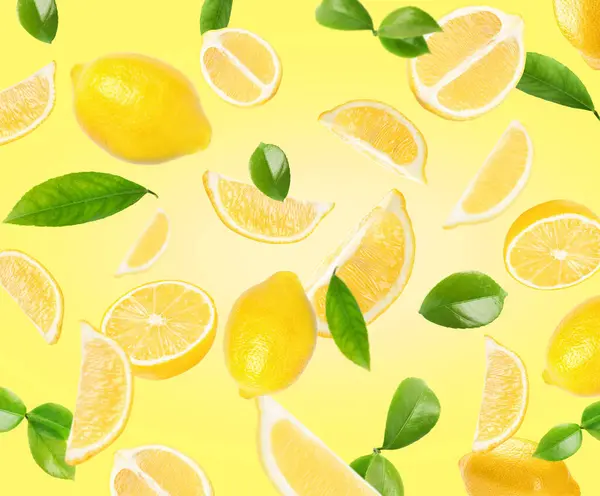 Fresh lemons and green leaves falling on light yellow background