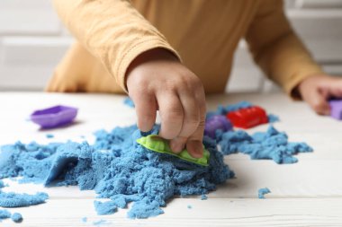 Küçük çocuk beyaz ahşap masada açık mavi kinetik kumla oynuyor, yakın plan.