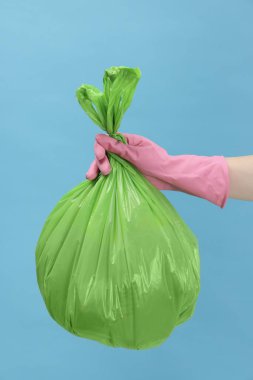 Açık mavi arka planda çöp dolu plastik poşet taşıyan kadın, yakın plan.