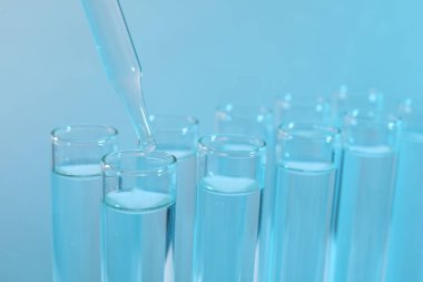 Laboratuvar analizi. Açık mavi arkaplanda test tüpüne damlayan ayıraç, yakın plan