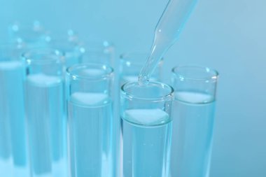 Laboratuvar analizi. Açık mavi arkaplanda test tüpüne damlayan ayıraç, yakın plan