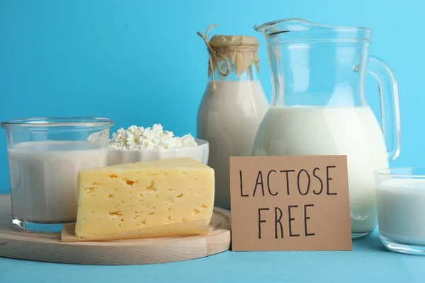 Dairy products and card with phrase Lactose Free on light blue table