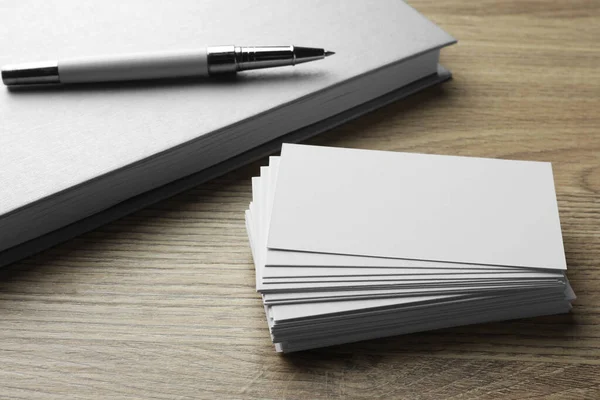 Stack of blank business cards, notebook and pen on wooden table. Mockup for design
