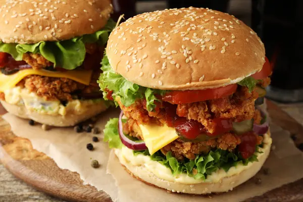 Delicious burgers with crispy chicken patty on wooden table, closeup
