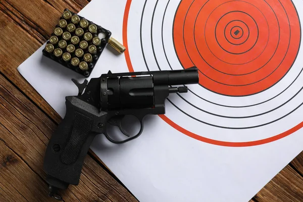 Shooting target, handgun and bullets on wooden table, top view