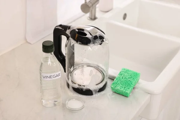 Cleaning electric kettle. Bottle of vinegar, sponge and baking soda on countertop in kitchen