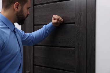 Mavi gömlekli tahsilat görevlisi ahşap kapıyı çalıyor.