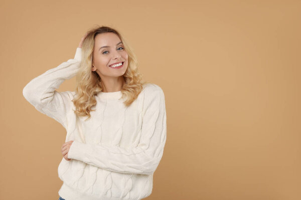 Happy woman in stylish warm sweater on beige background. Space for text