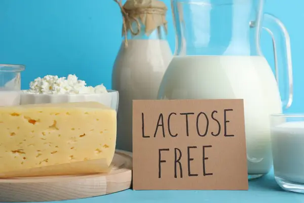 Dairy products and card with phrase Lactose Free on light blue table, closeup