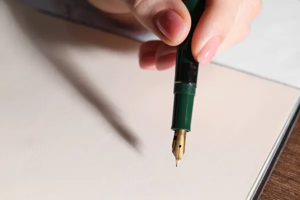 Woman writing with fountain pen at table, closeup