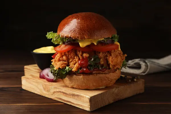 Delicious burger with crispy chicken patty on wooden table