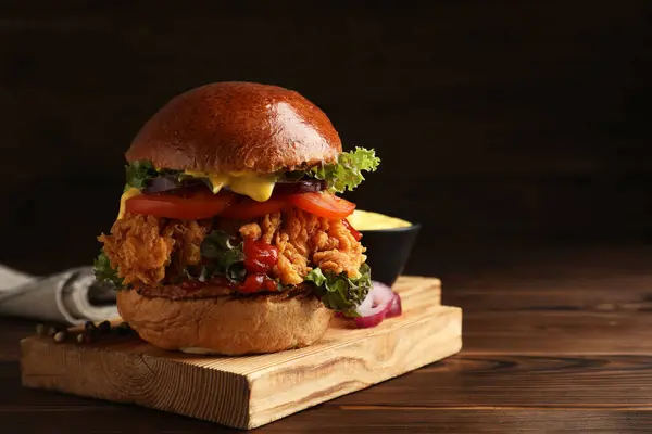 Delicious burger with crispy chicken patty on wooden table. Space for text