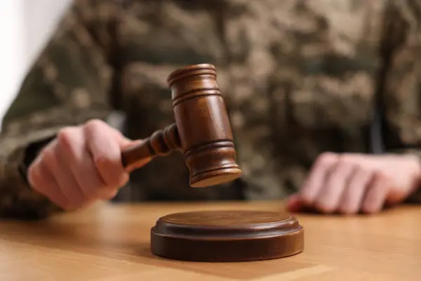 Law concept. Man in military uniform with gavel at wooden table, closeup