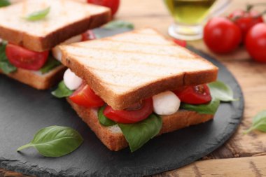 Nefis Caprese sandviçleri, mozarella, domates, fesleğen ve pesto sosu ahşap masada, yakın plan.