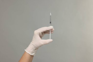 Gri arka planda tıbbi şırınga tutan doktor, yakın plan.