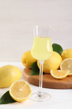 Lezzetli limoncello, limon ve yeşil yapraklı beyaz ahşap masa.