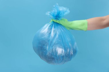 Açık mavi arka planda çöp dolu plastik poşet taşıyan kadın, yakın plan.