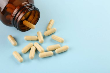 Açık mavi arka planda şişe ve vitamin kapsülleri, yakın plan. Metin için boşluk