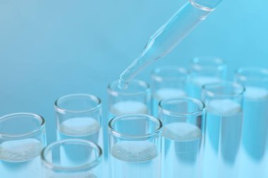 Laboratuvar analizi. Açık mavi arkaplanda test tüpüne damlayan ayıraç, yakın plan