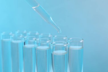 Laboratuvar analizi. Açık mavi arkaplanda test tüpüne damlayan ayıraç, yakın plan