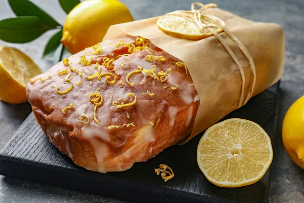 Wrapped tasty lemon cake with glaze and citrus fruits on grey table, closeup