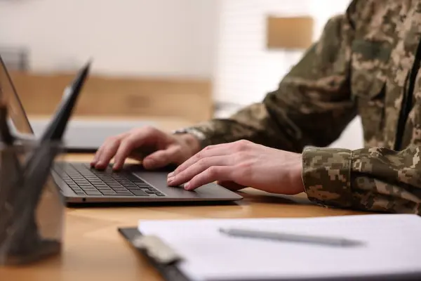 Military service. Soldier working with laptop at wooden table indoors, closeup