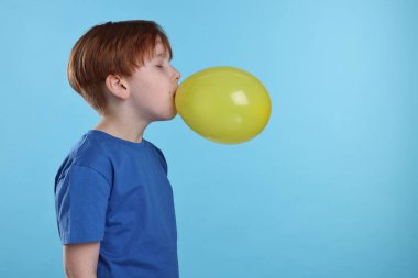 Açık mavi arka planda sarı balon şişiren çocuk