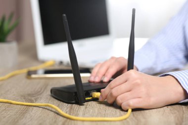 Bir kadın ahşap masadaki kablosuz internet yönlendiricisine ethernet kablosu yerleştiriyor.