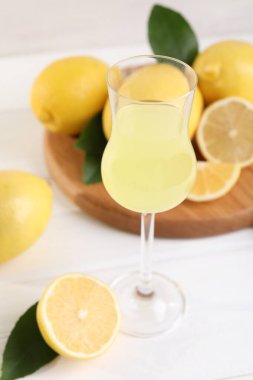 Lezzetli limoncello, limon ve yeşil yapraklı likör bardağı beyaz ahşap masada, yakın plan.