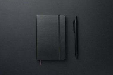 Siyah arkaplan üzerinde kapalı defter ve kalem, üst görünüm