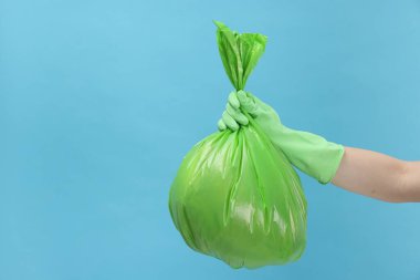 Açık mavi arka planda çöp dolu plastik poşet taşıyan bir kadın, yakın plan. Metin için boşluk