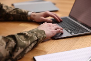 Askerlik. Asker ahşap masada dizüstü bilgisayarla çalışıyor, yakın plan.