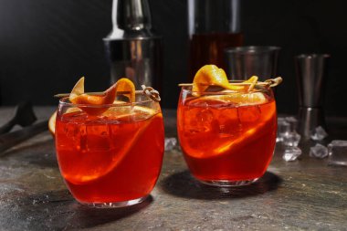 Aperol sprey kokteyli, buz küpleri ve gri desenli masada portakal dilimleri.