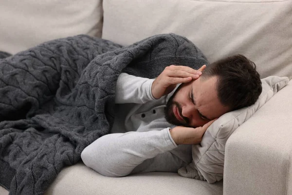 Man suffering from headache on sofa under blanket
