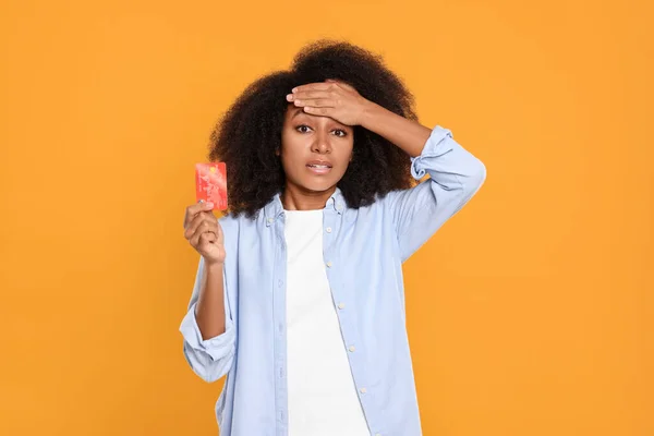 Confused woman with credit card on orange background. Debt problem