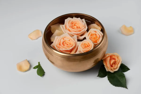 Tibetan singing bowl with water and beautiful rose flowers on white background
